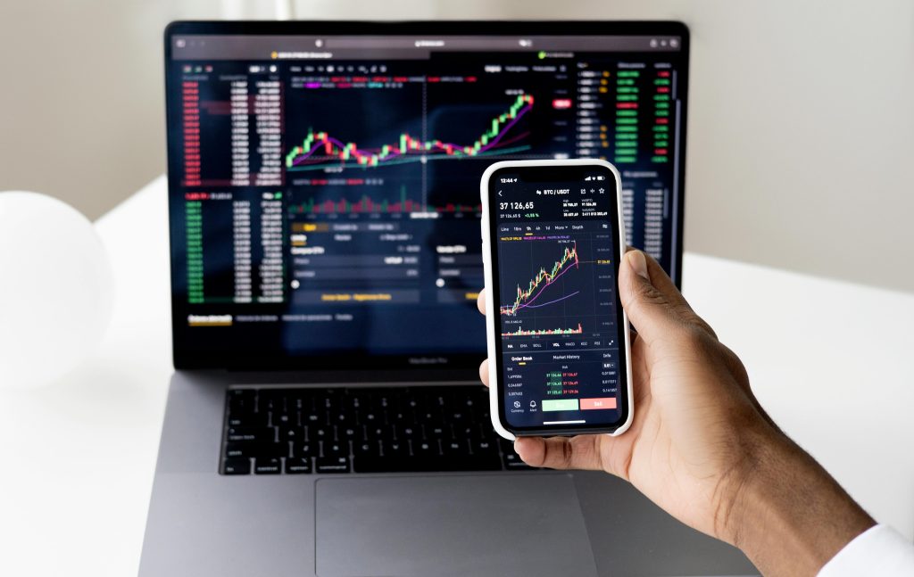 pexels-photo-6802042-6802042 Person checking stock market graphs on laptop and smartphone, focusing on financial data.